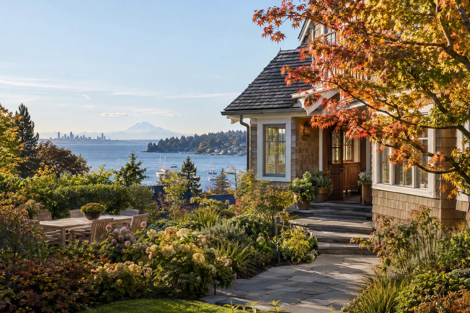 Shingle-style island home with a cottage garden and a teak table in Bainbridge Island, Washington, with Eagle Harbor near Winslow with sailboats and the faint Seattle skyline across Puget Sound