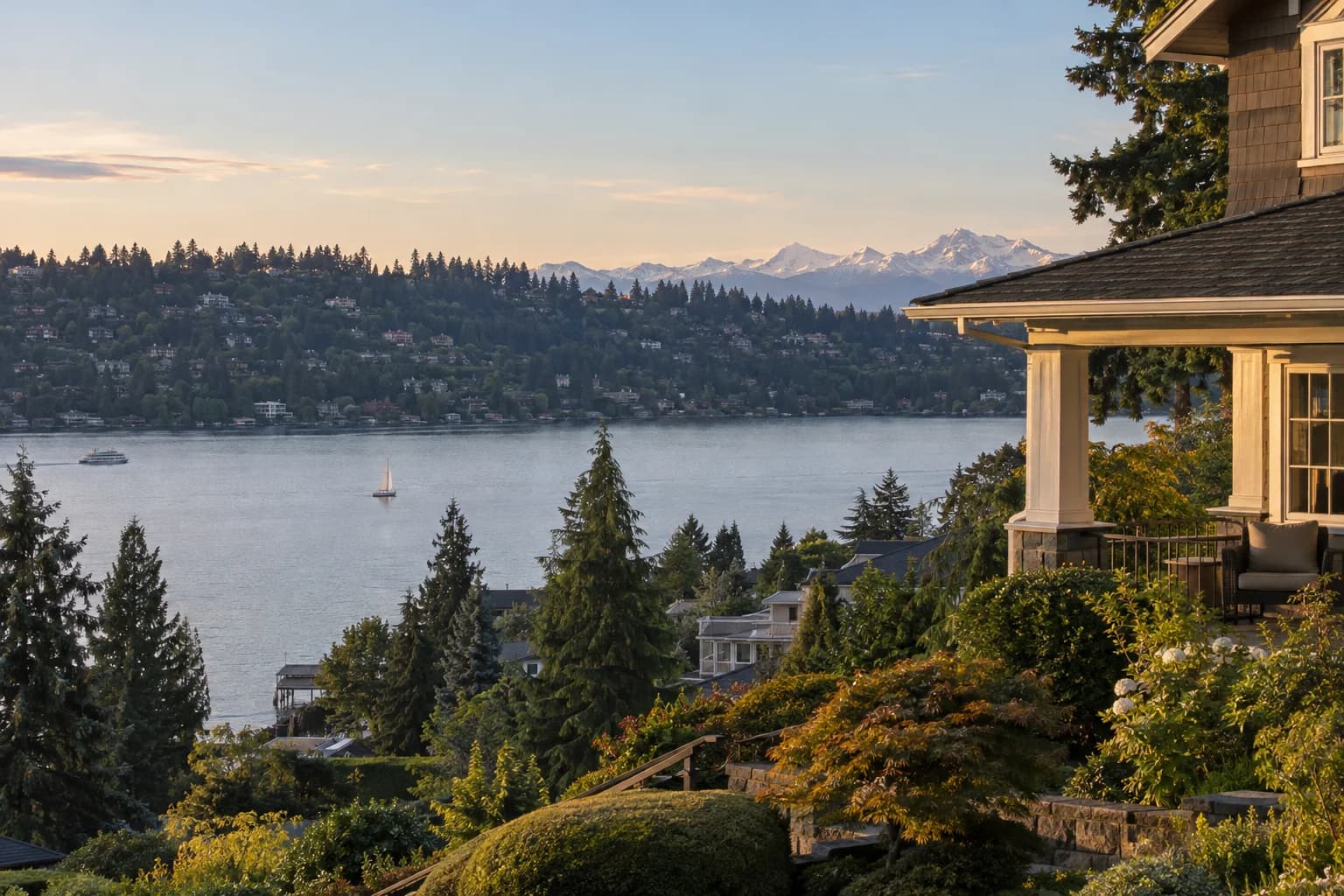 Classic craftsman on a hill with a porch in King County, Washington, above Lake Washington with a residential hillside of homes among evergreens on the far shore and the Cascade Mountains beyond