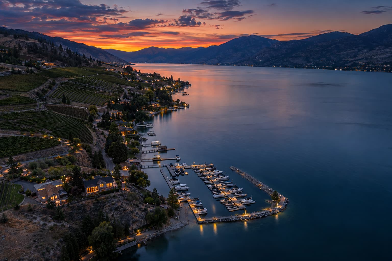 Aerial view of Lake Chelan's south shore at dusk with vineyards, docks and scattered homes lit against the dry hills