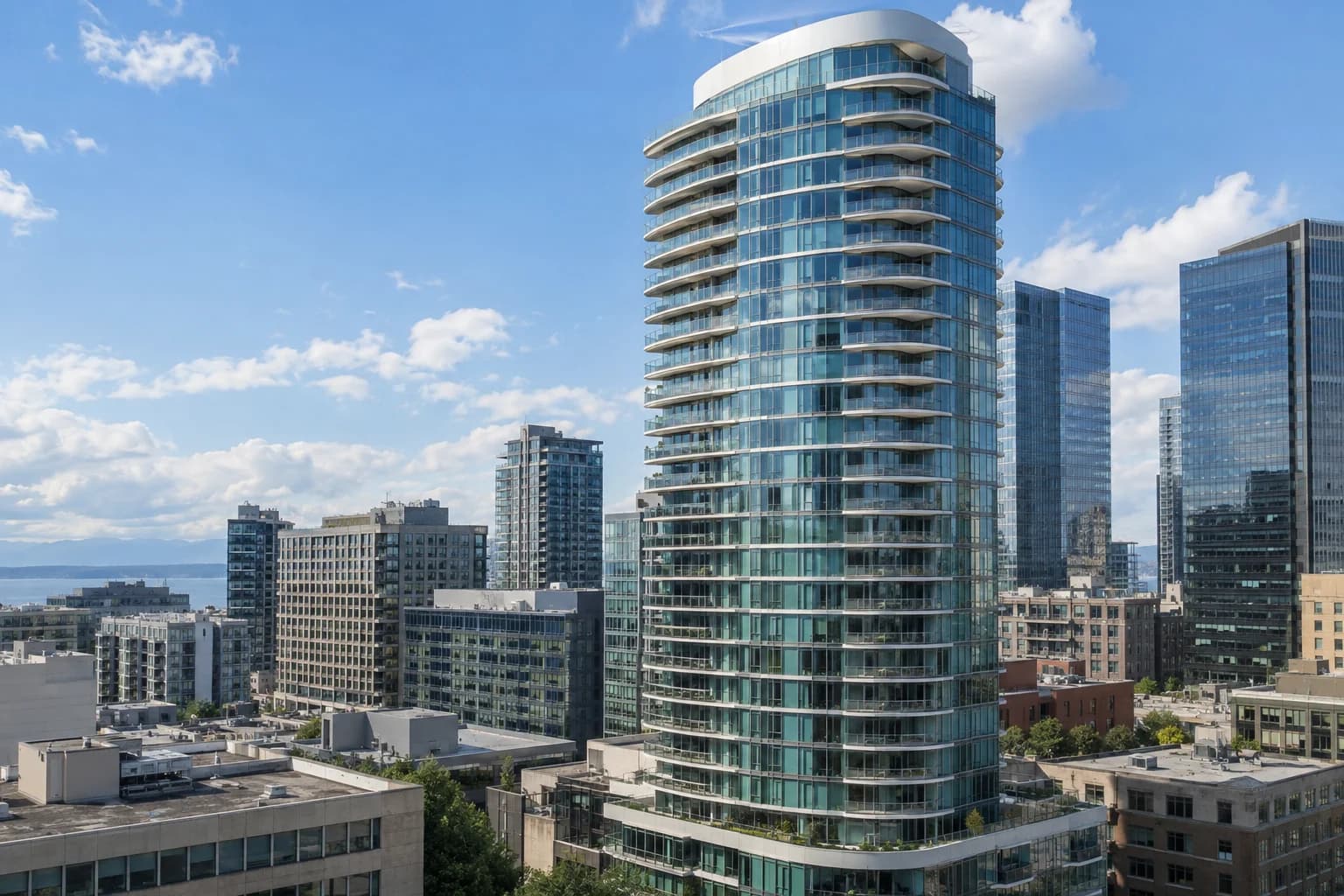Curved blue-green glass residential tower with stacked balconies and a white crown in downtown Seattle — RexMont Real Estate