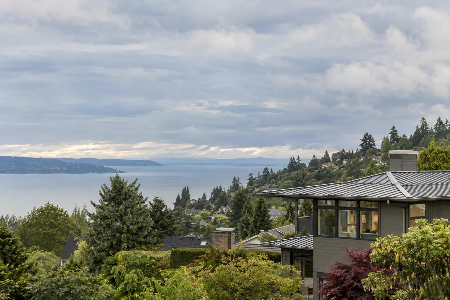 Regional Eastside neighborhood establishing shot with evergreen hills and residential rooftops in Seattle — RexMont Real Estate